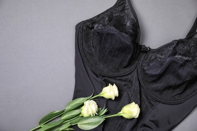 Photo of Elegant black plus size women's underwear and beautiful eustoma flowers on grey background, top view. Space for text