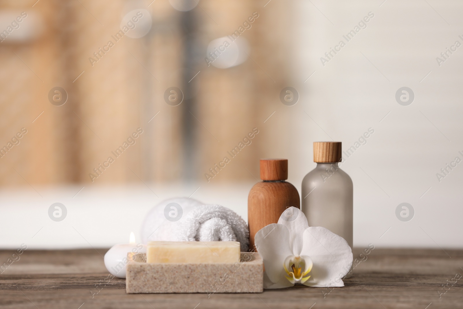 Photo of Composition with spa products, beautiful flower and candle on wooden table against blurred background, space for text