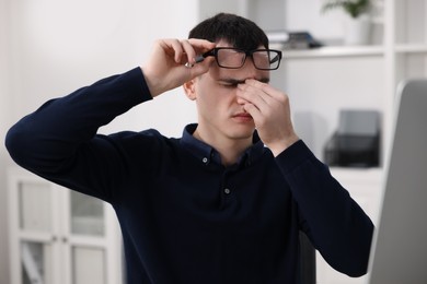 Photo of Young man with glasses suffering from headache in office