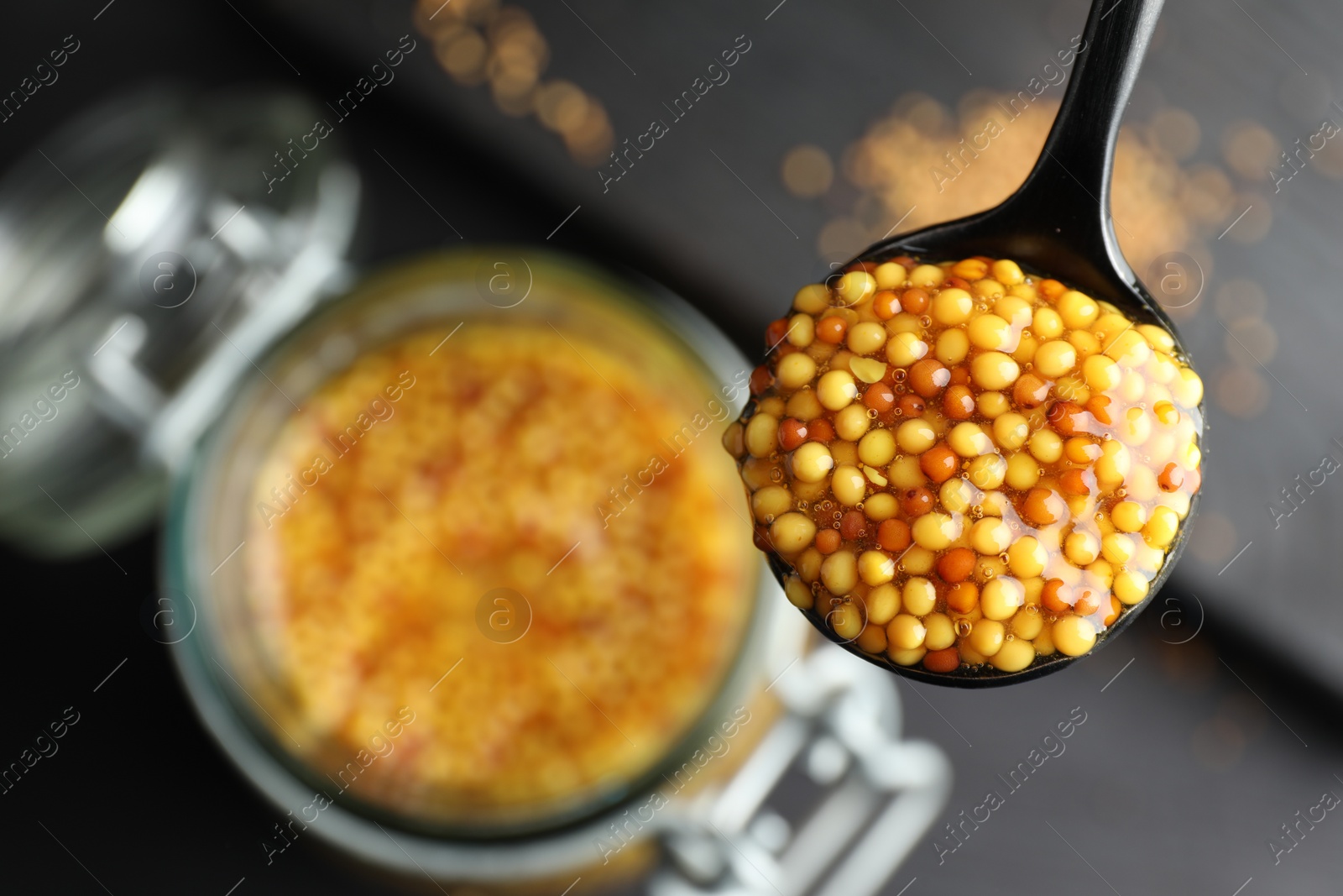 Photo of Spoon with whole grain mustard over jar on table, closeup