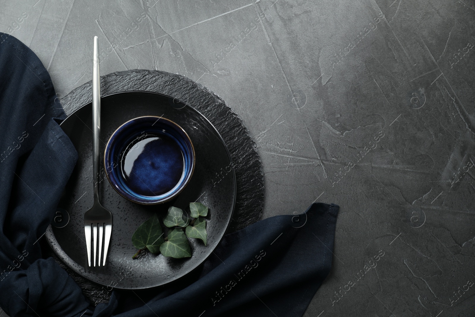 Photo of Stylish table setting. Dishes, fork, napkin and green leaves on grey surface, top view with space for text