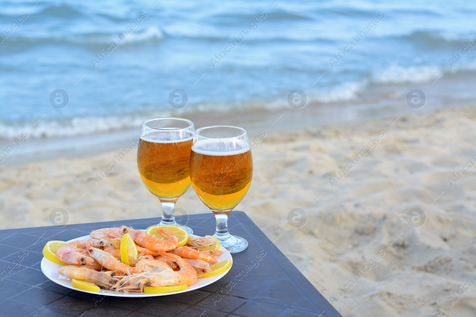 Photo of Cold beer in glasses and shrimps served with lemon on beach