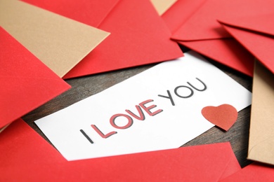 Card with phrase I Love You, red heart and envelopes on wooden table, closeup