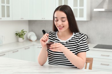 Happy woman with tasty yogurt in kitchen