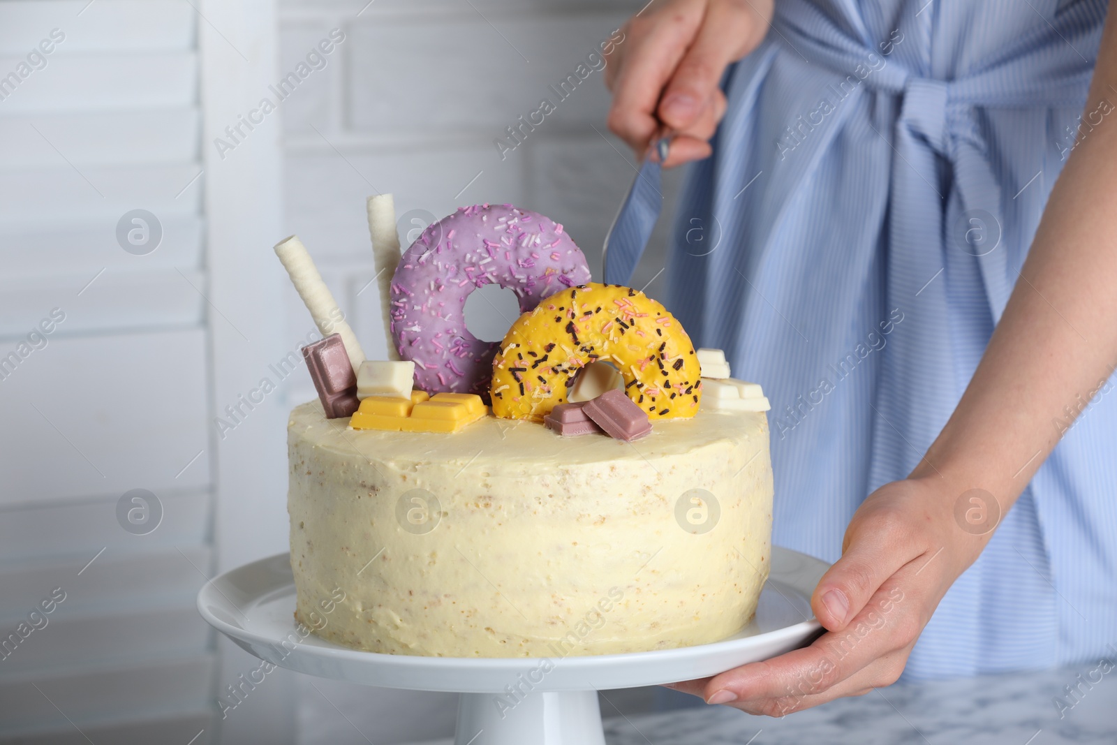 Photo of Woman cutting delicious cake decorated with sweets at table, closeup