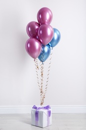 Photo of Bright balloons and gift box on floor against white wall