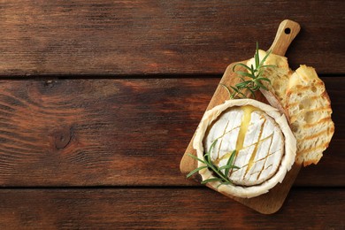 Photo of Board with tasty baked brie cheese, bread and rosemary on wooden table, top view. Space for text