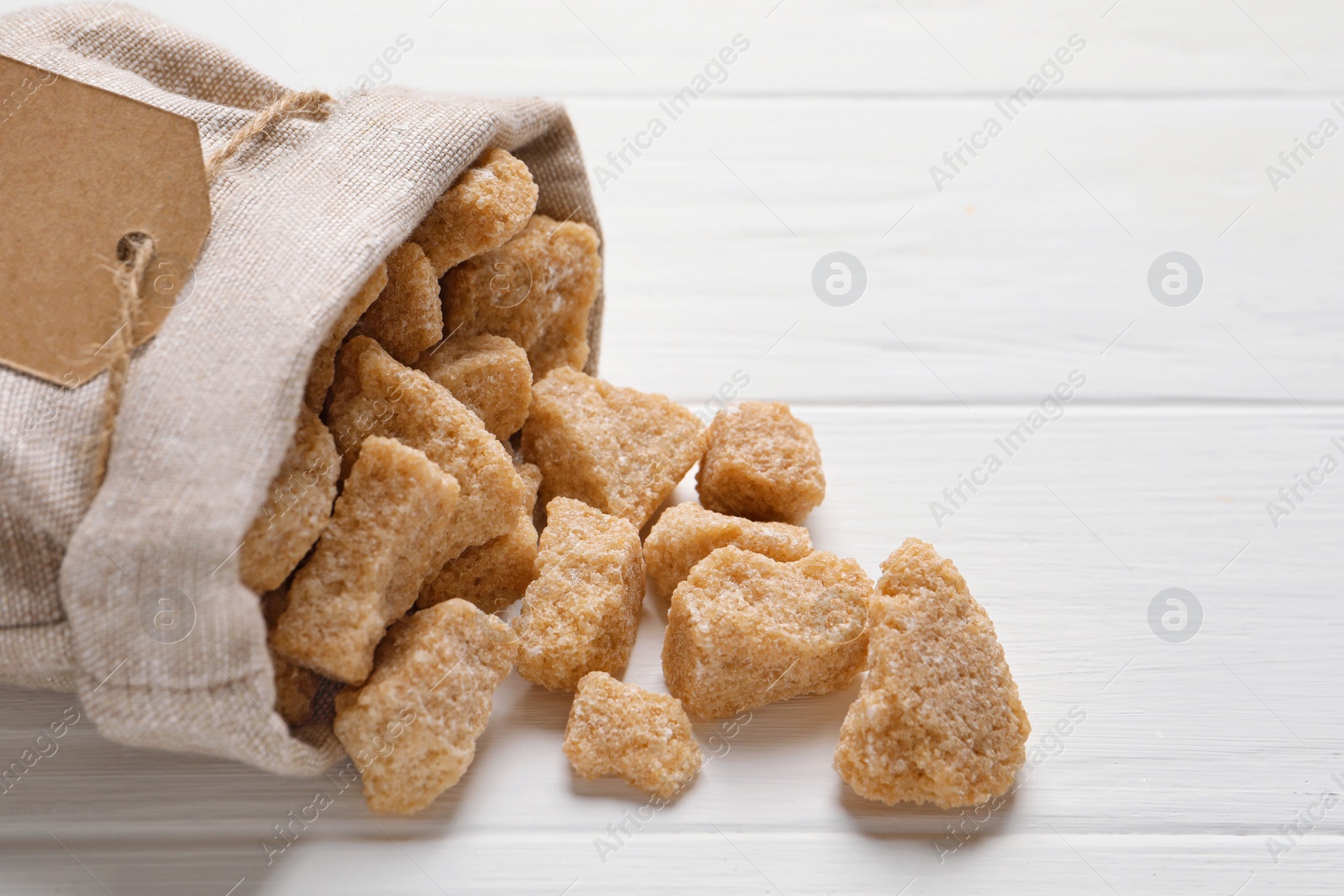 Photo of Bag of brown sugar pieces on white wooden table, closeup. Space for text