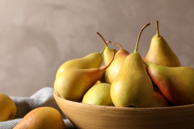 Photo of Bowl with ripe pears on table against grey background