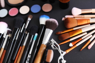 Photo of Different makeup brushes and cosmetic products on black background