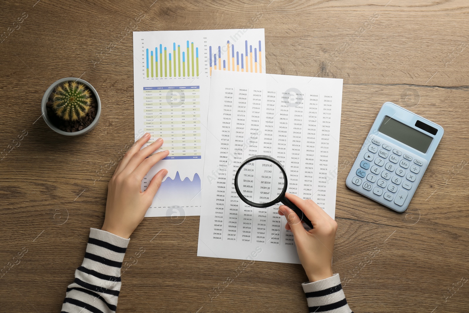 Photo of Woman looking at accounting document through magnifying glass at wooden table, top view