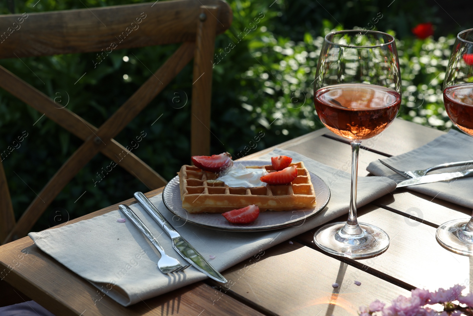 Photo of Delicious Belgian waffles with fresh strawberries and wine served on table in spring garden