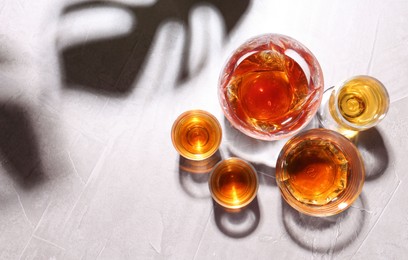 Photo of Many different liqueurs in glasses on light table, flat lay. Space for text