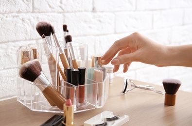 Woman taking lipstick from organizer for makeup cosmetic products on dressing table