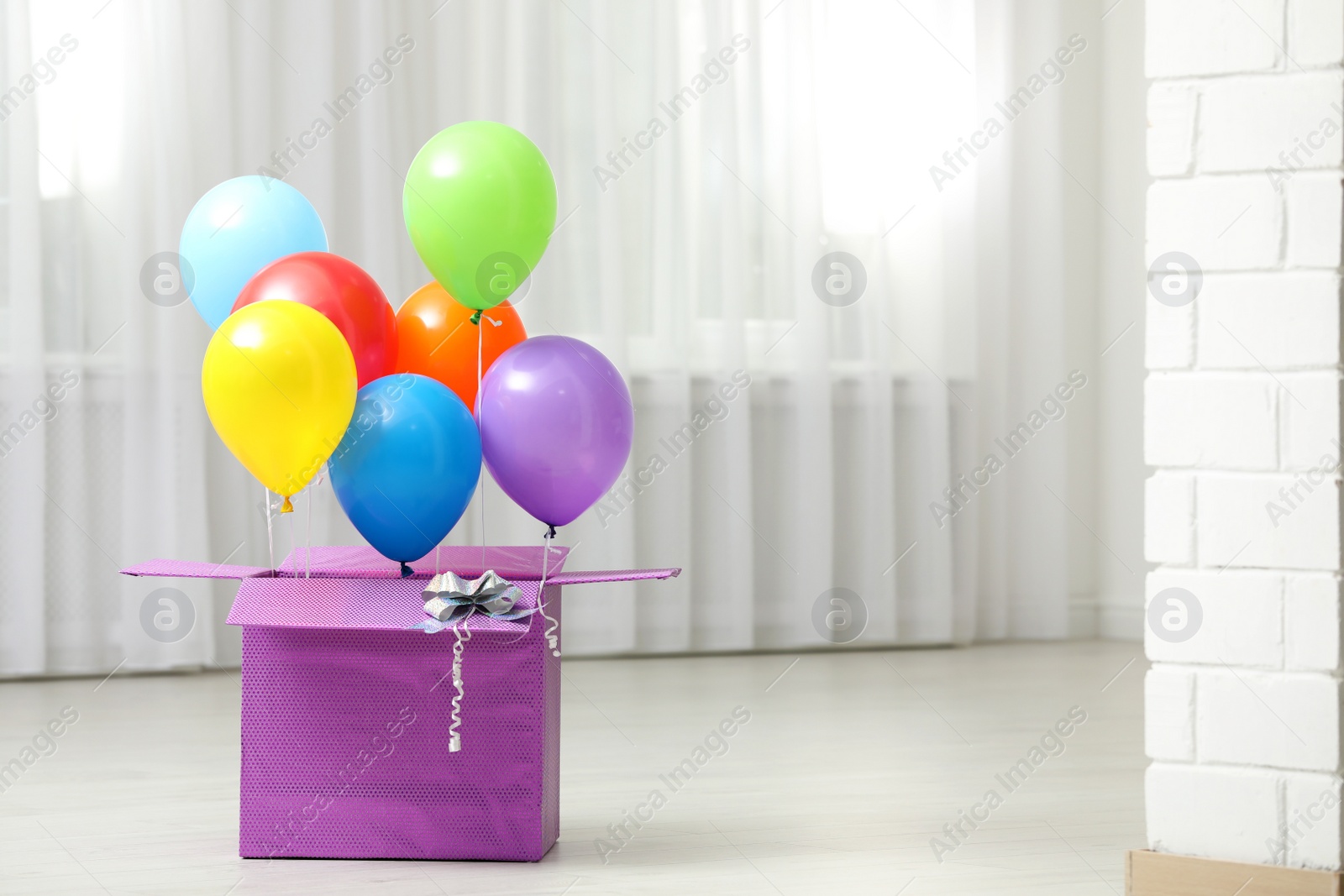 Photo of Gift box with bright air balloons on floor indoors. Space for text