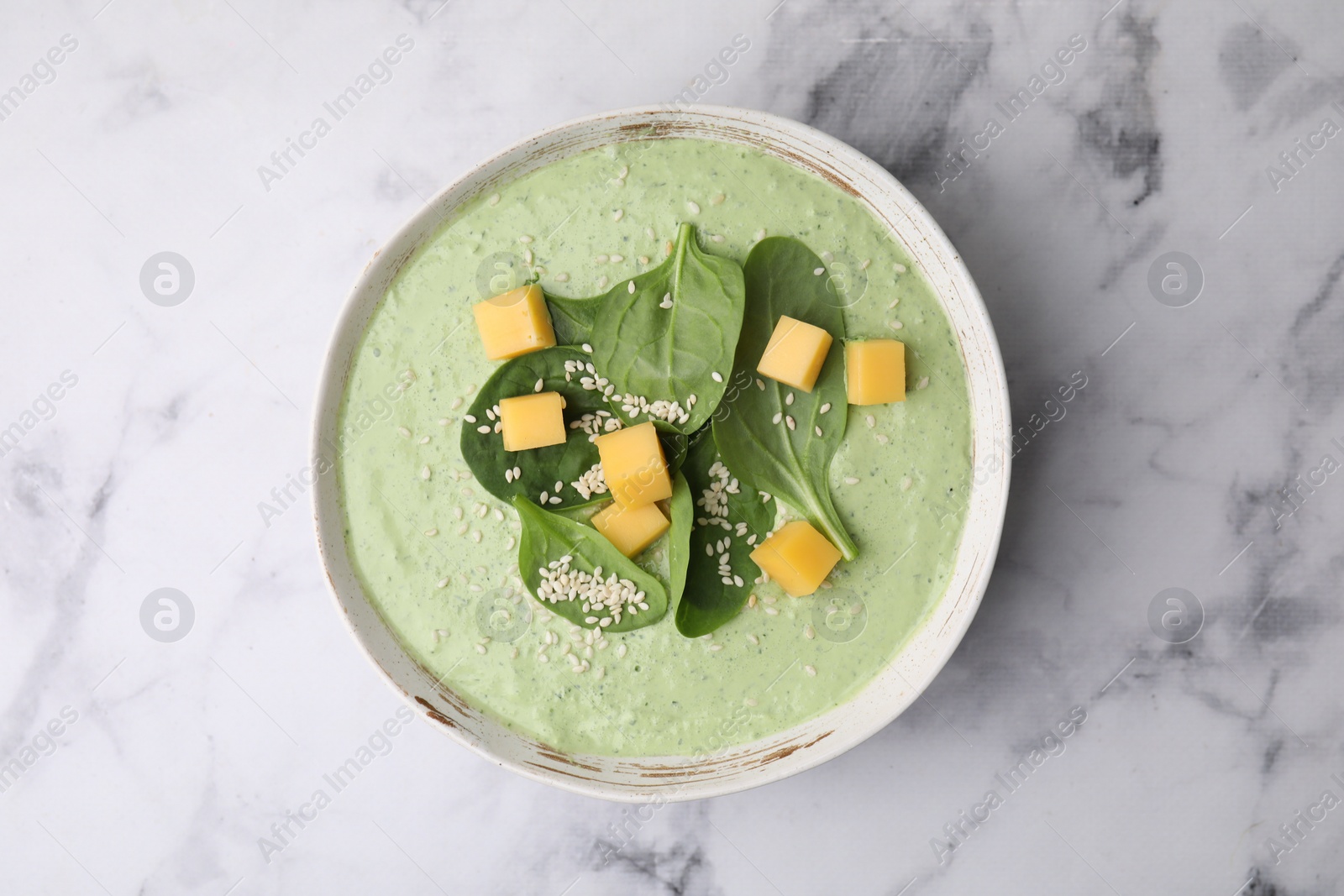 Photo of Delicious spinach cream soup with cheese and sesame seeds in bowl on white marble table, top view