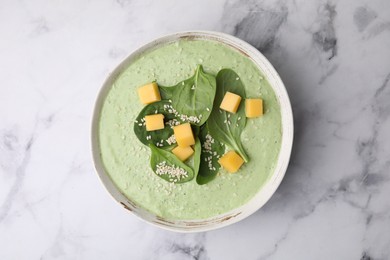 Photo of Delicious spinach cream soup with cheese and sesame seeds in bowl on white marble table, top view