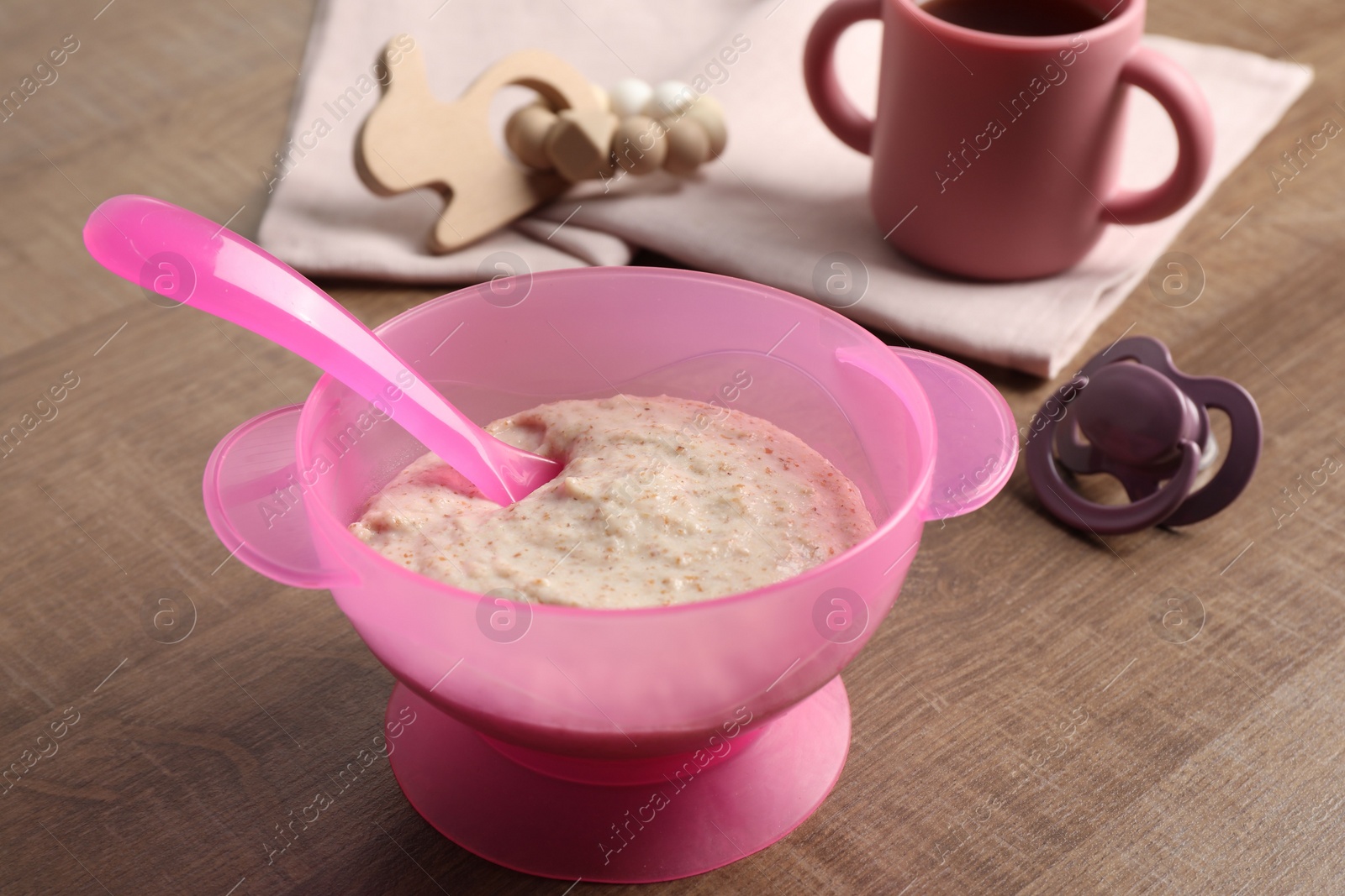 Photo of Baby food. Puree in bowl, drink, toy and soother on wooden table