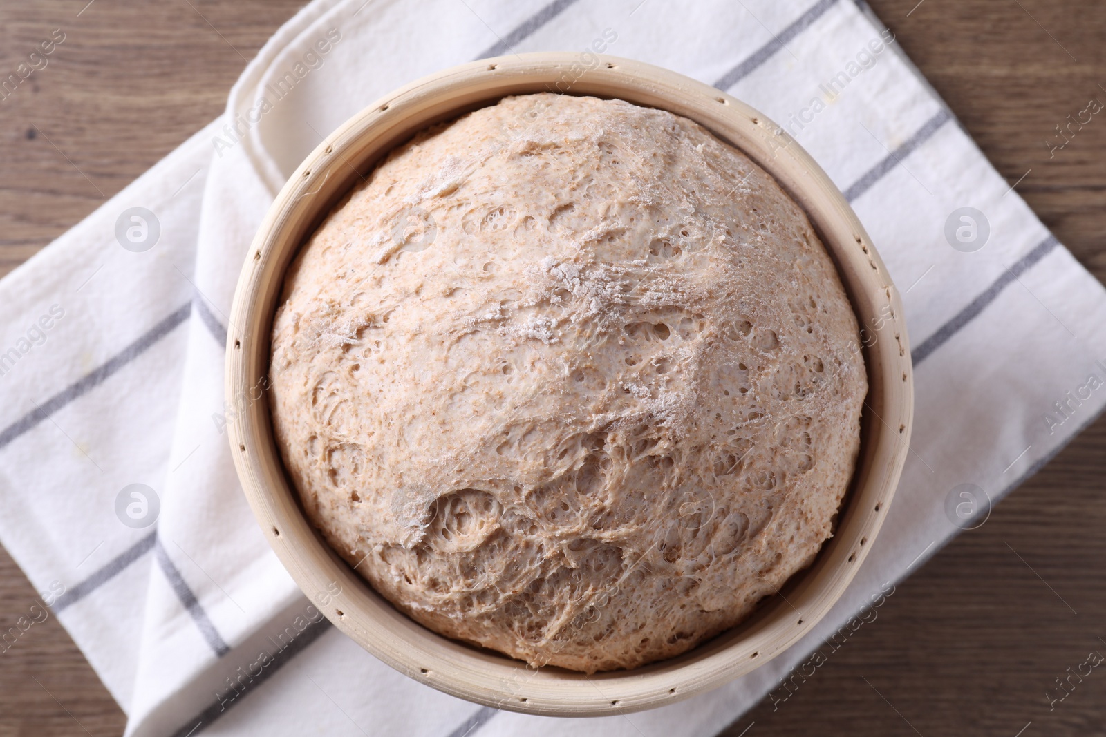 Photo of Fresh sourdough in proofing basket on wooden table, top view