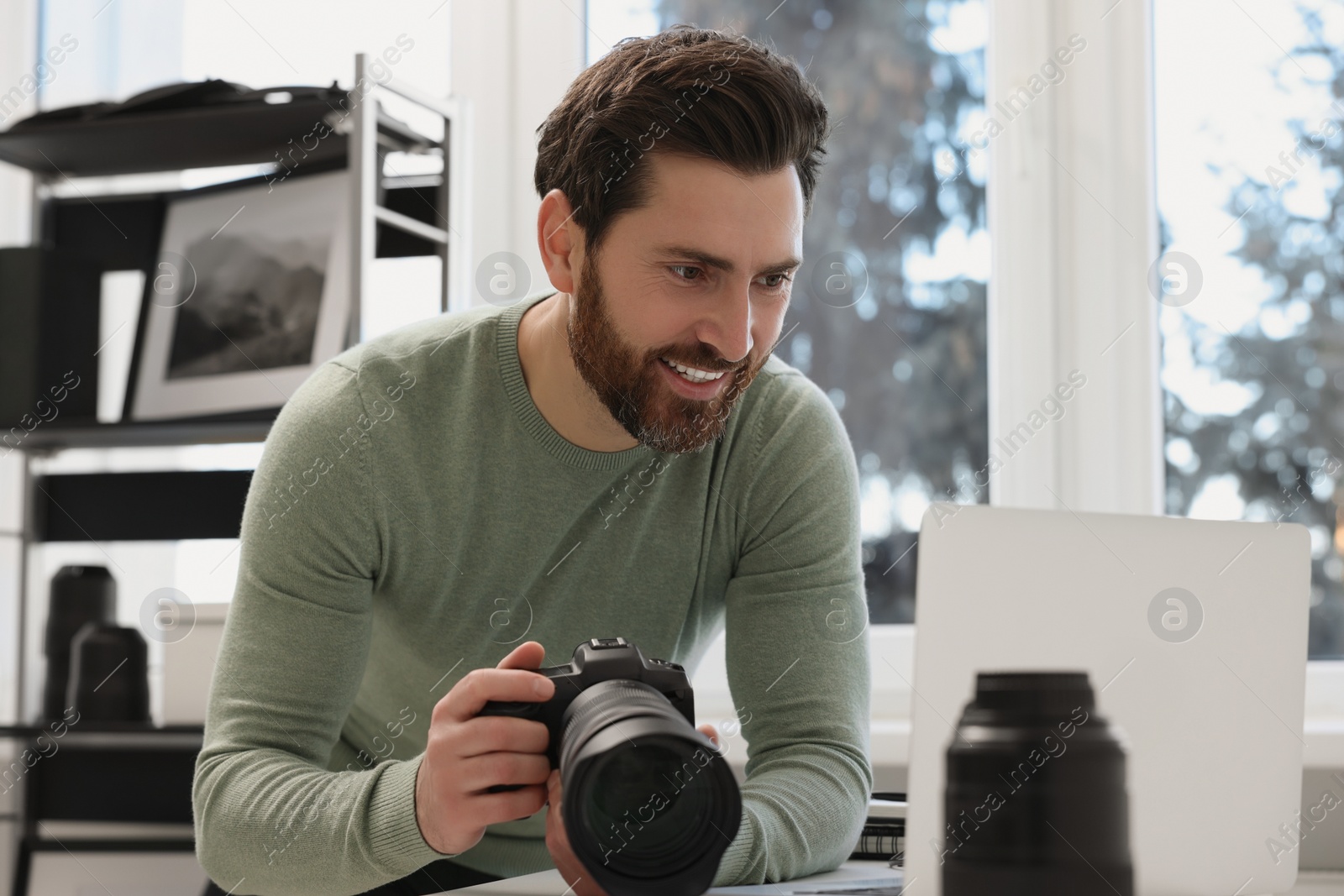 Photo of Professional photographer holding digital camera near table with laptop indoors