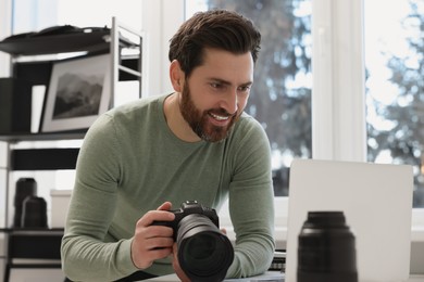 Photo of Professional photographer holding digital camera near table with laptop indoors