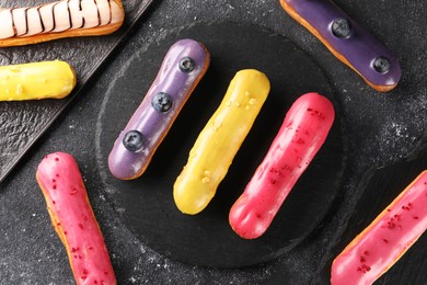 Photo of Different tasty glazed eclairs on dark textured table, flat lay