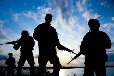 Silhouettes of soldiers with assault rifles patrolling outdoors. Military service
