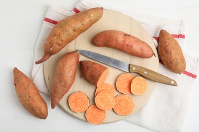 Photo of Whole and cut ripe sweet potatoes on white wooden table, flat lay