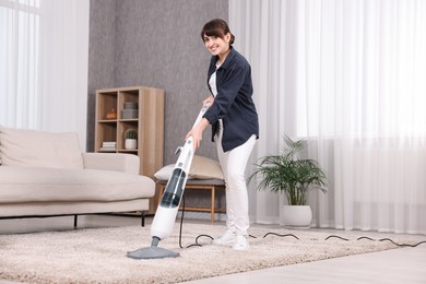 Happy young housewife vacuuming carpet at home