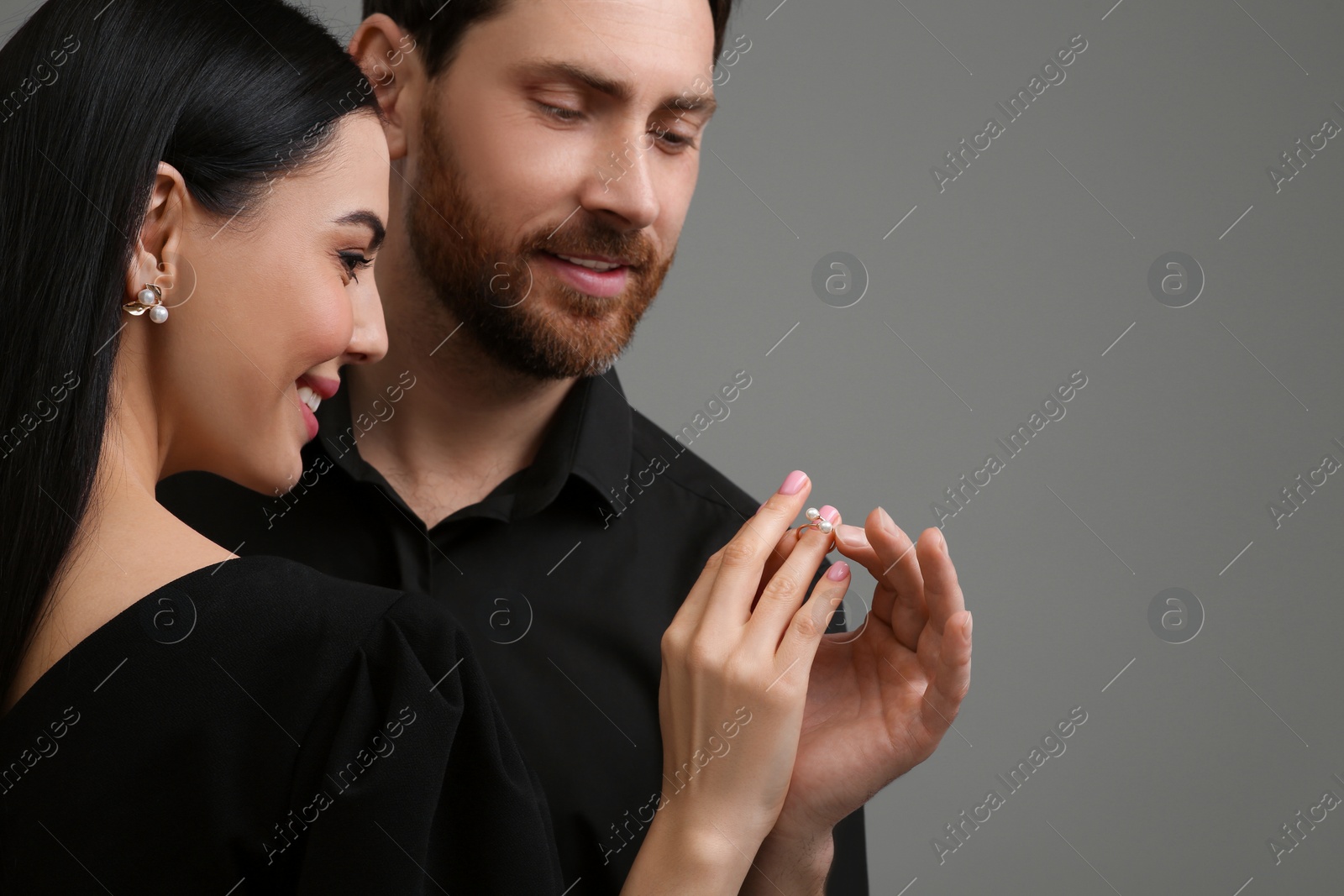 Photo of Man putting elegant ring on woman's finger against dark grey background, closeup