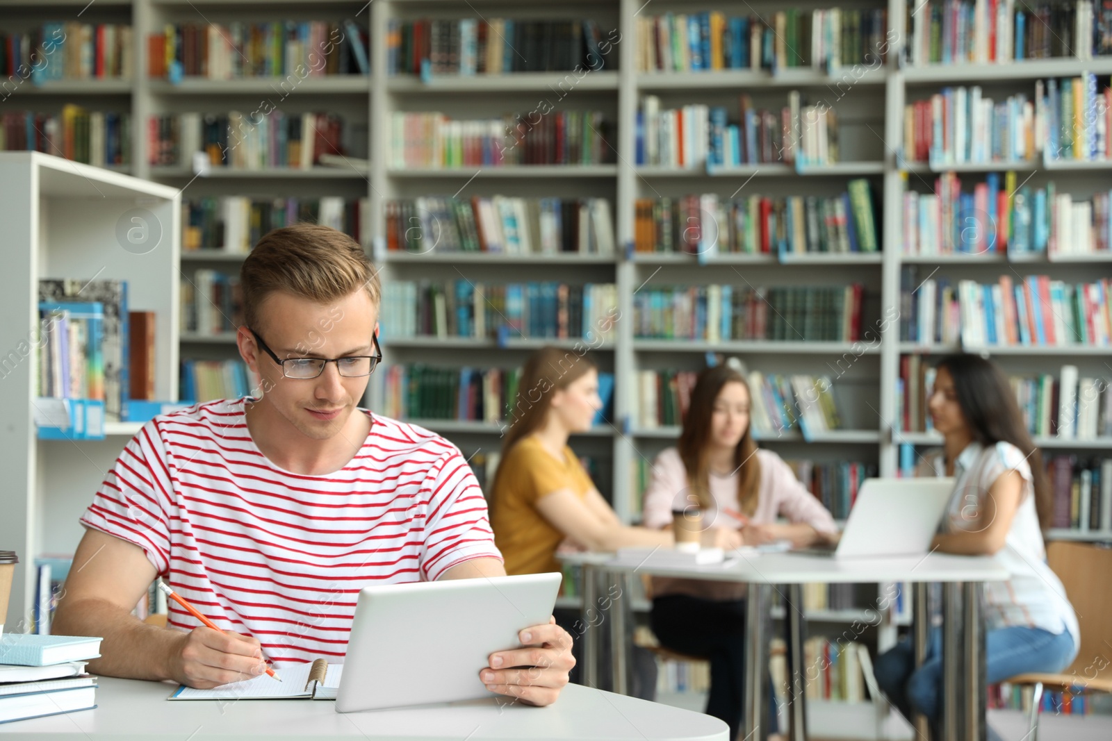 Photo of Young man studying with tablet at table in library. Space for text