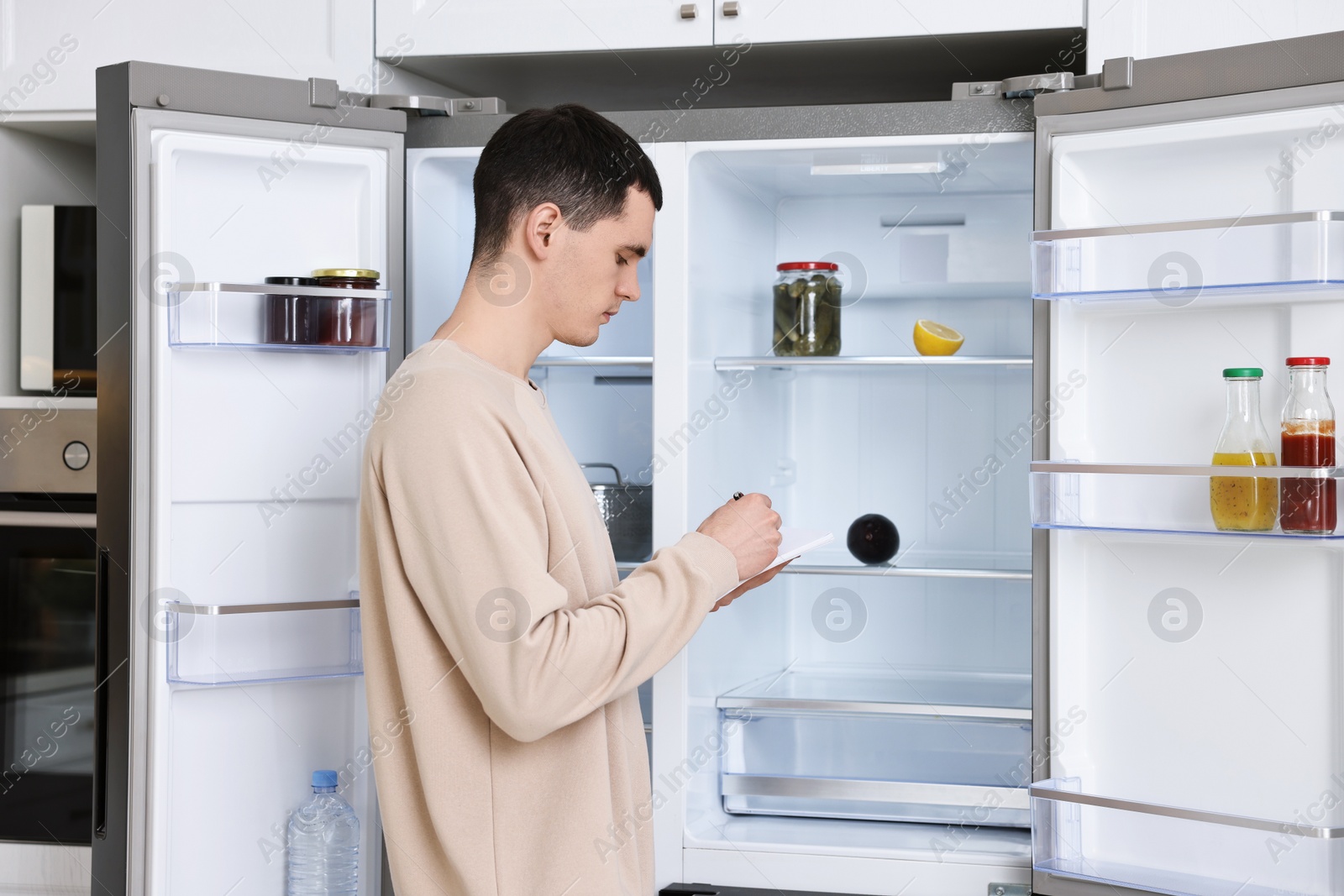 Photo of Man writing notes near empty refrigerator in kitchen