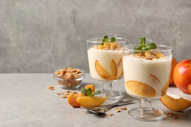 Photo of Tasty peach yogurt with granola, mint and pieces of fruits on light grey table, space for text