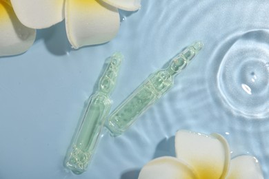 Skincare ampoules and beautiful plumeria flowers in water on light blue background, flat lay