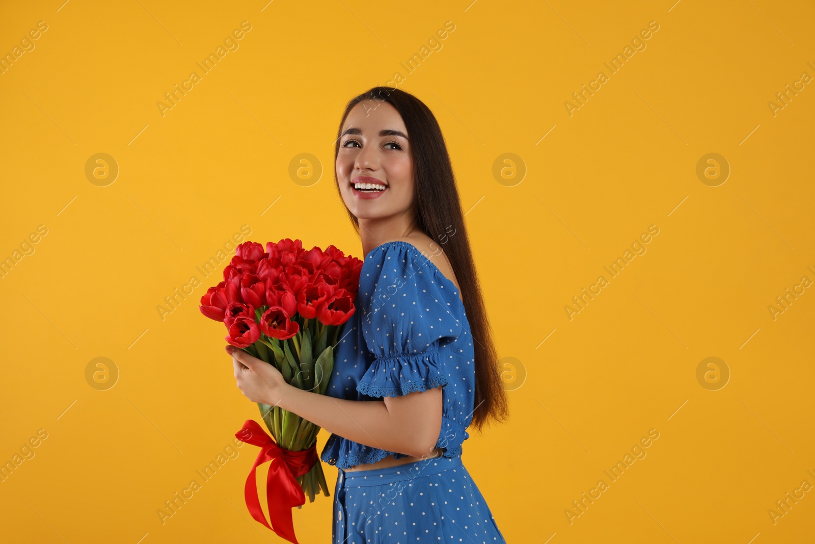 Photo of Happy woman with red tulip bouquet on yellow background. 8th of March celebration