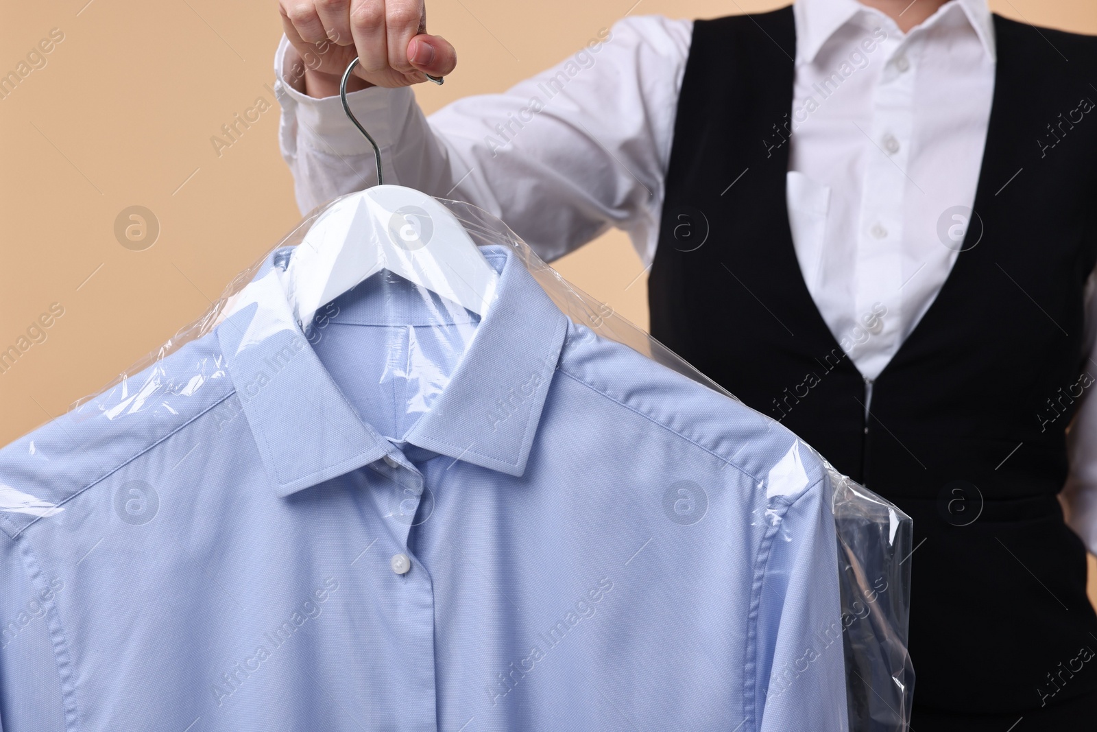 Photo of Dry-cleaning service. Woman holding shirt in plastic bag on beige background, closeup