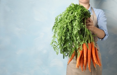 Photo of Woman holding fresh ripe carrots against color background. Space for text