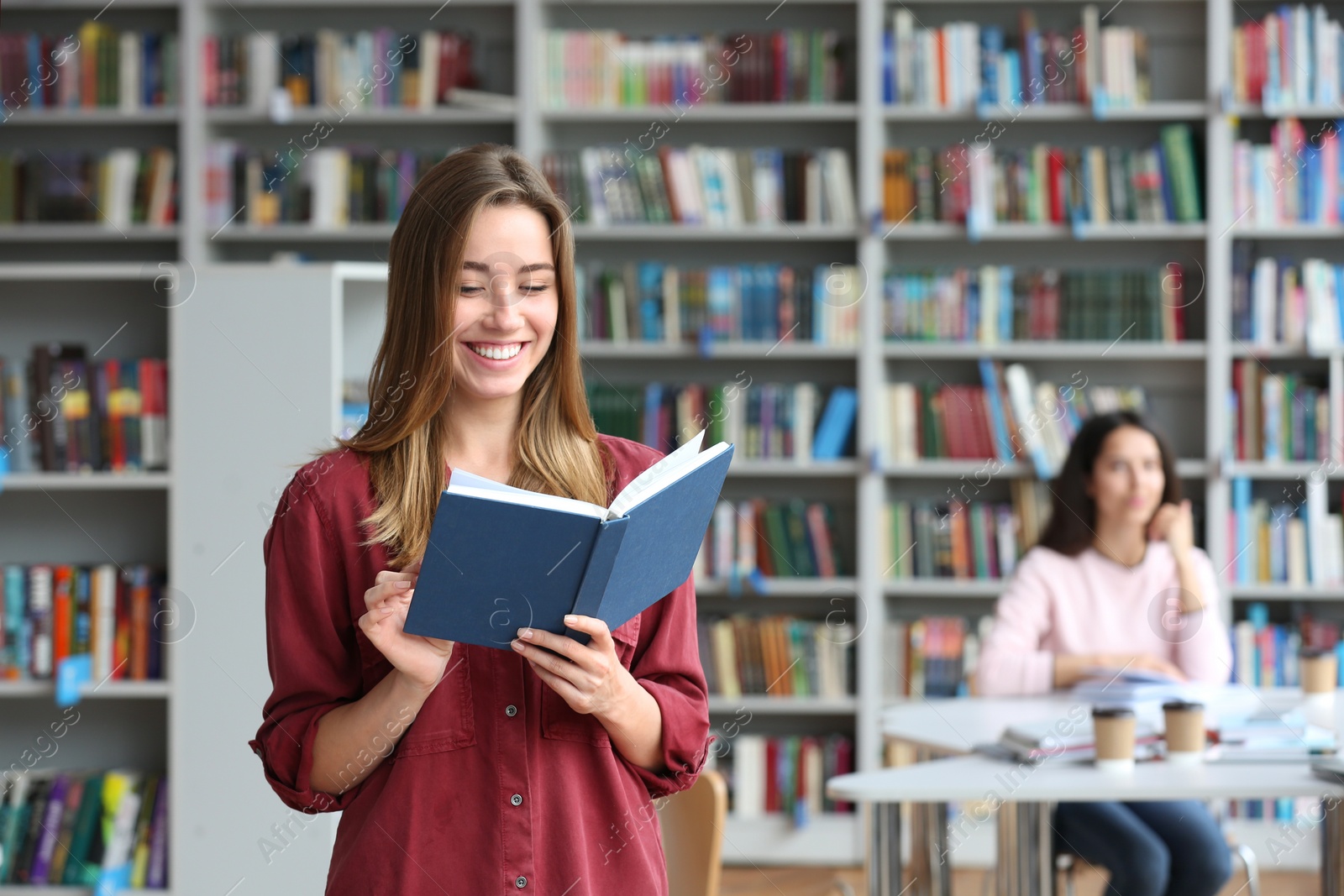 Photo of Young pretty woman reading book in library. Space for text