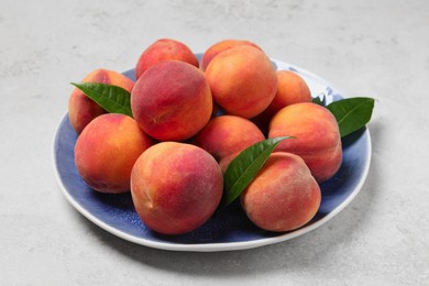 Photo of Many whole fresh ripe peaches and green leaves in plate on white table, closeup