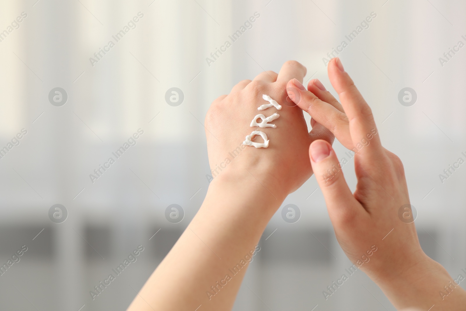 Photo of Young woman with word Dry made of cream on her hand indoors, closeup. Space for text