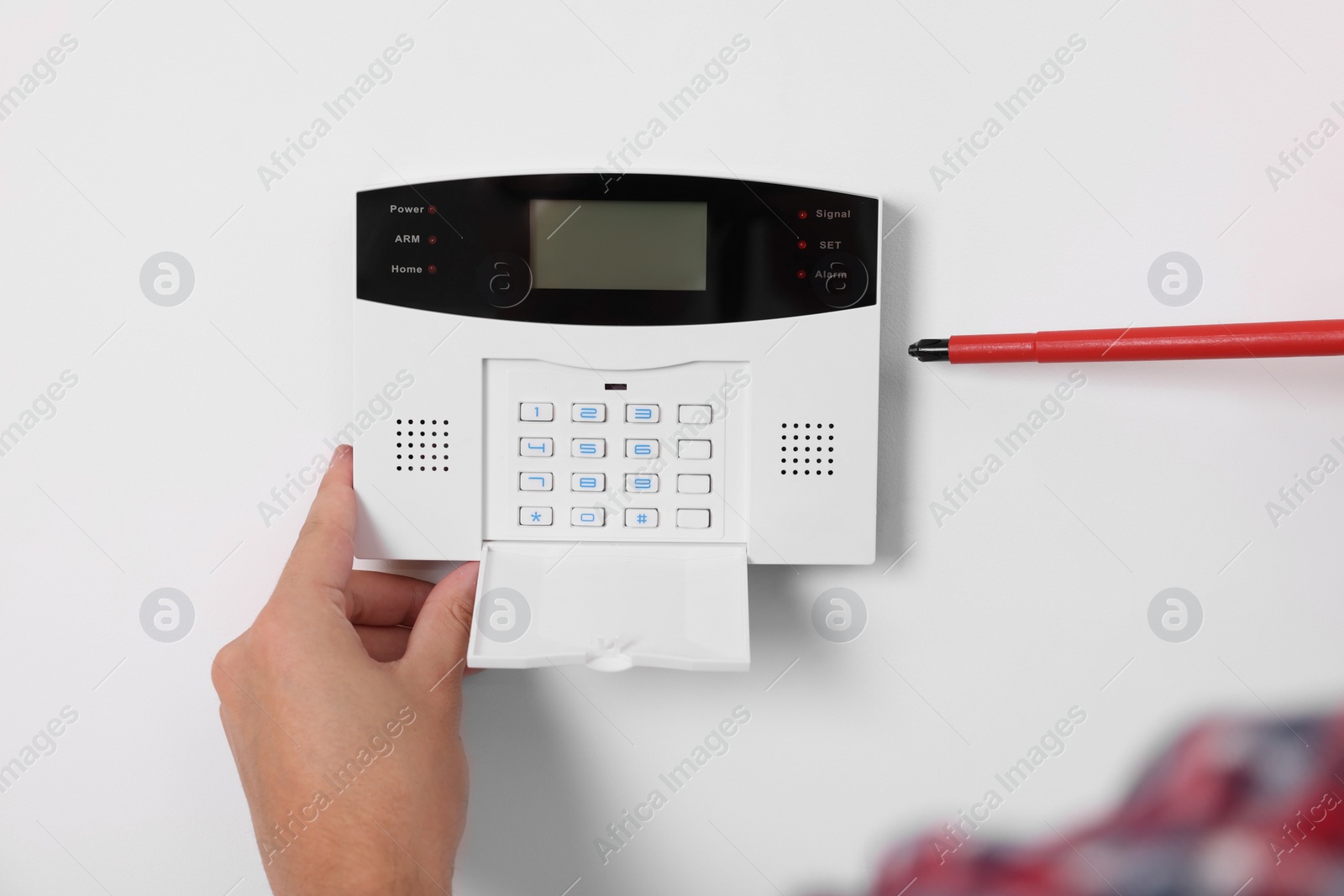 Photo of Man installing home security alarm system on white wall indoors, closeup