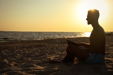 Young man reading book on sandy beach near sea