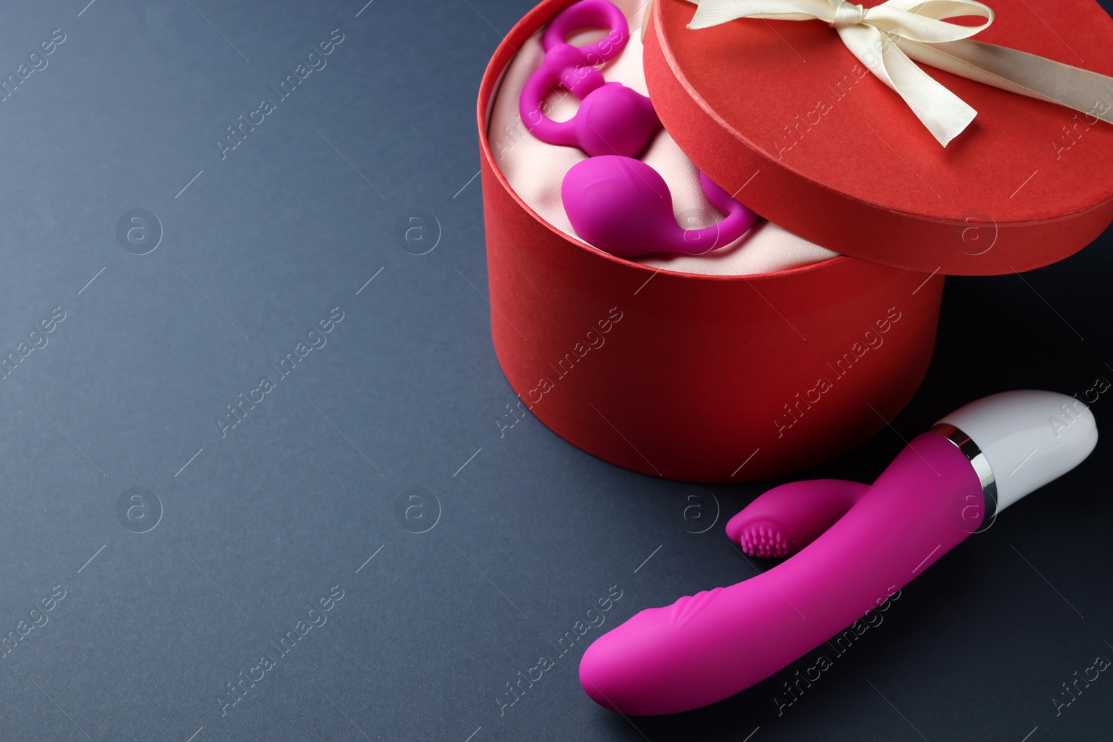 Photo of Pink sex toys and gift box on dark blue background, space for text