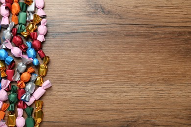 Photo of Many candies in colorful wrappers on wooden table, flat lay. Space for text