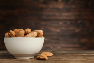 Ceramic bowl with almonds on wooden table, space for text. Cooking utensil