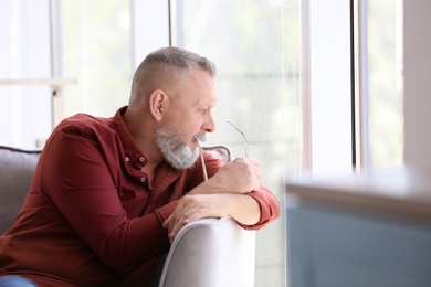 Photo of Depressed senior man sitting in armchair indoors