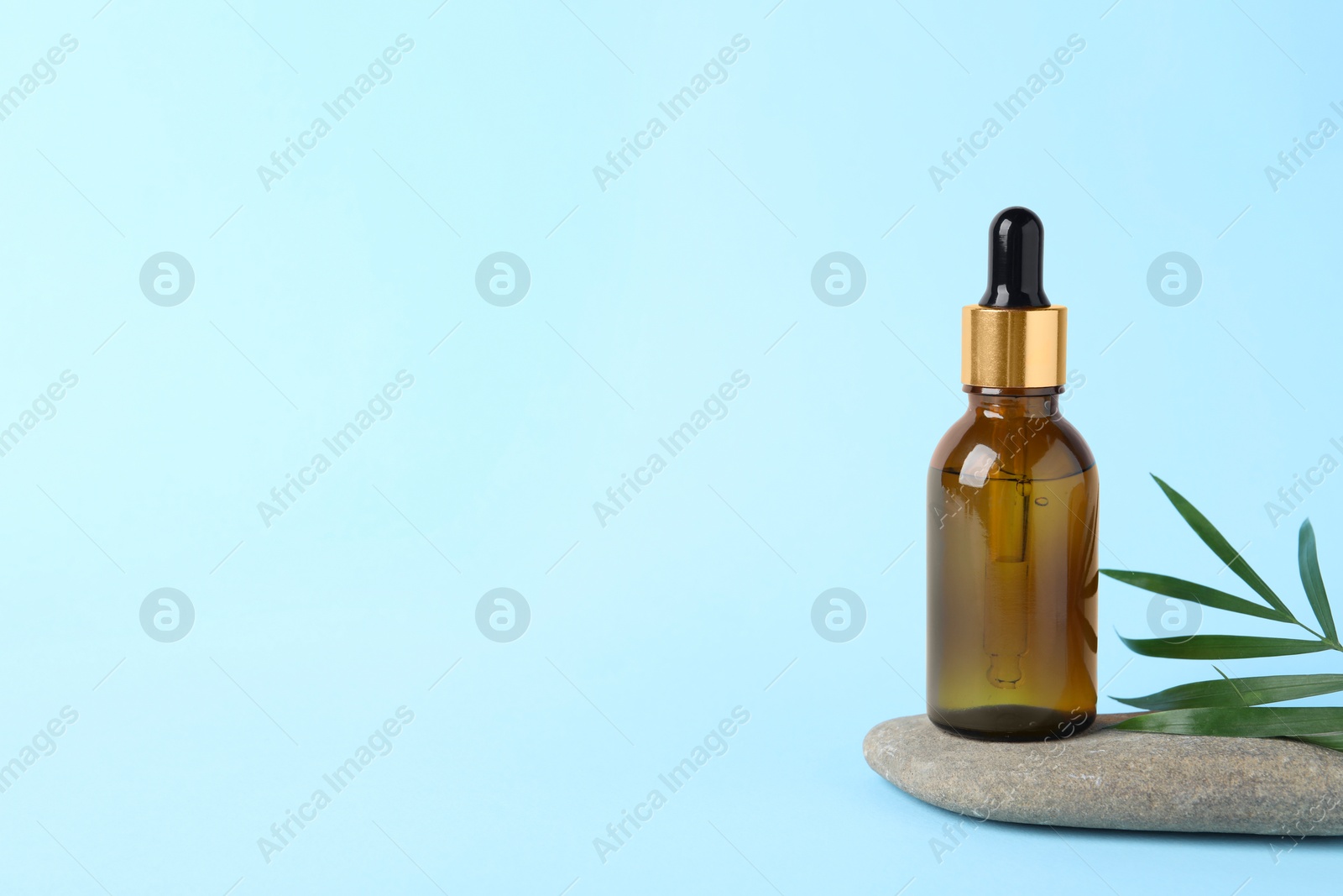 Photo of Bottle with cosmetic oil, stone and green leaf on light blue background, space for text