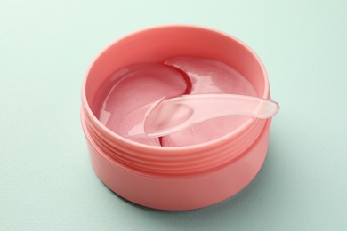 Photo of Jar of under eye patches with spoon on turquoise background, closeup. Cosmetic product
