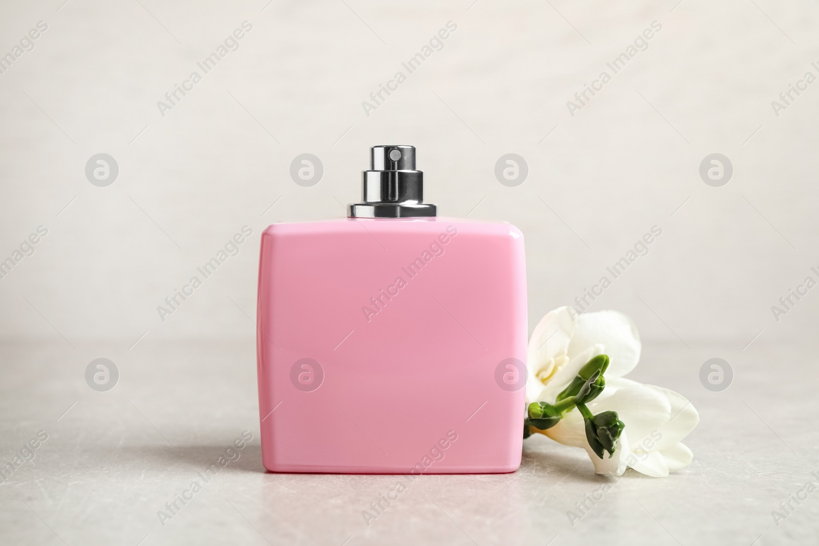 Photo of Bottle of perfume and beautiful freesia flower on light table