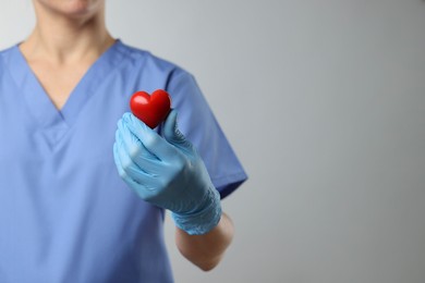 Doctor wearing light blue medical glove holding decorative heart on grey background, closeup. Space for text